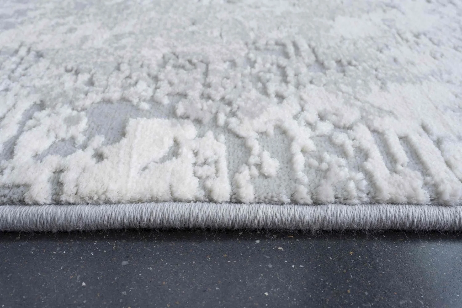 Tepih YON 6484 svijetli apstraktni tepih u ivory, srebrnosivim i svijetlosivim tonovima, izrađen od 55% poliestera i 45% heatset polipropilena, s reljefnom teksturom.